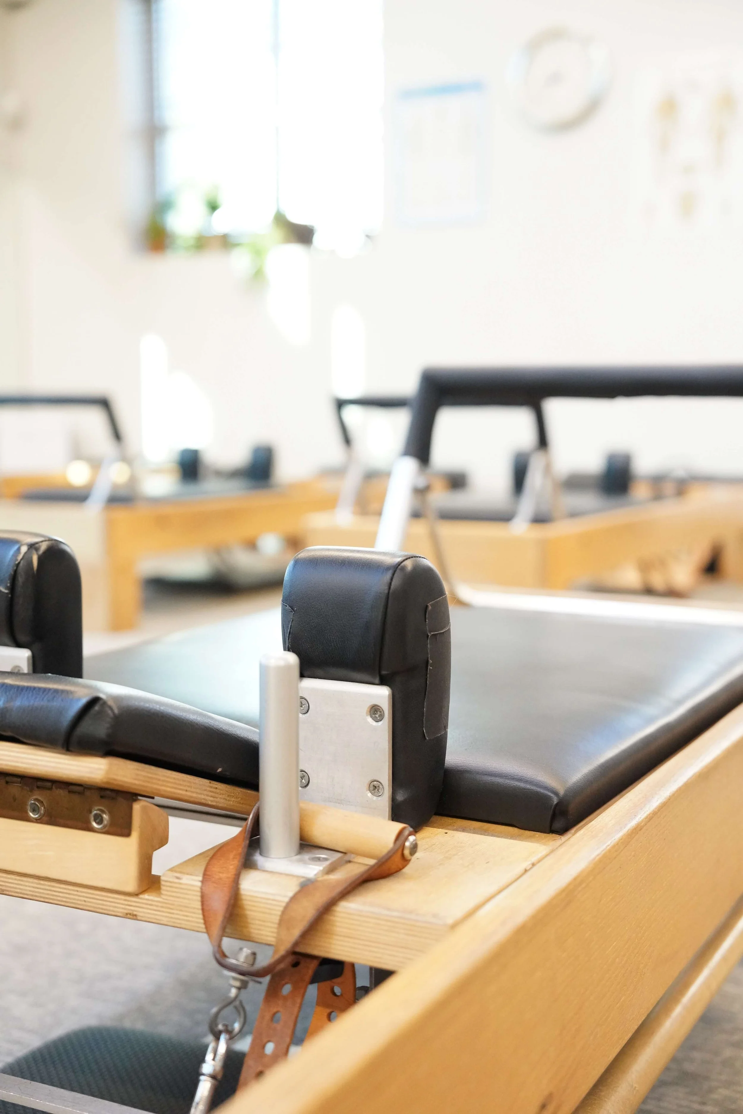 A Pilates reformer machine in a fitness studio with a black padded surface, wooden frame, and metal components, set up for exercising.