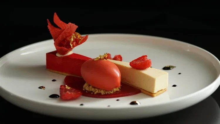 Elegant plated dessert with red and white chocolate elements, garnished with red fruit and gold leaf, served on a white dish