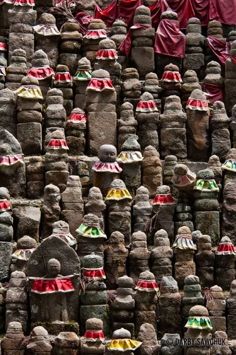 A large collection of small stone Jizo statues, some wearing red, yellow, and green cloth accessories.