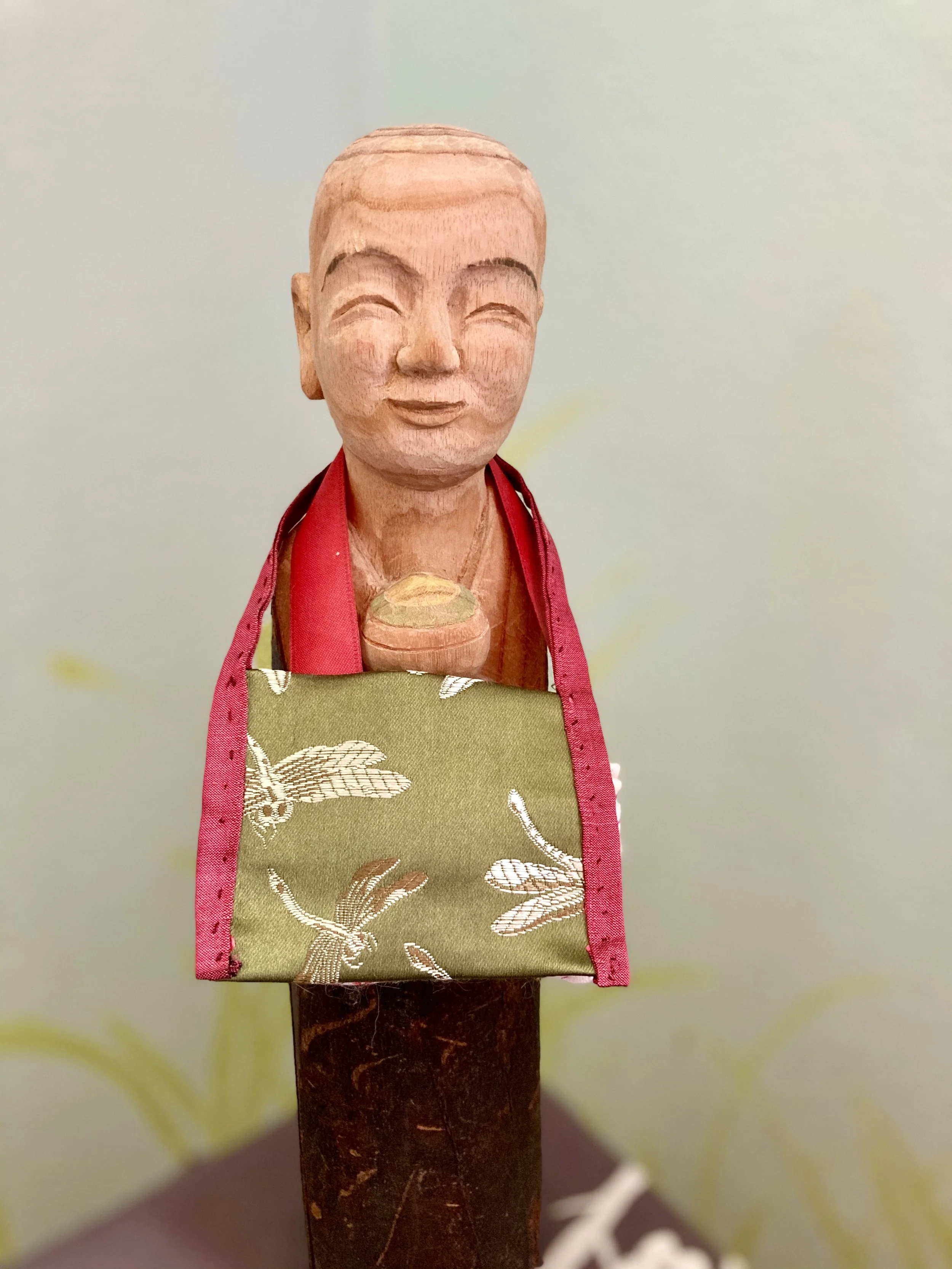 A wooden statue of a smiling child wearing a red apron with a floral pattern, displayed on a stand.