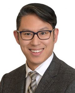 Portrait of a smiling man wearing glasses, a gray suit, white shirt, and a striped tie, against a white background.