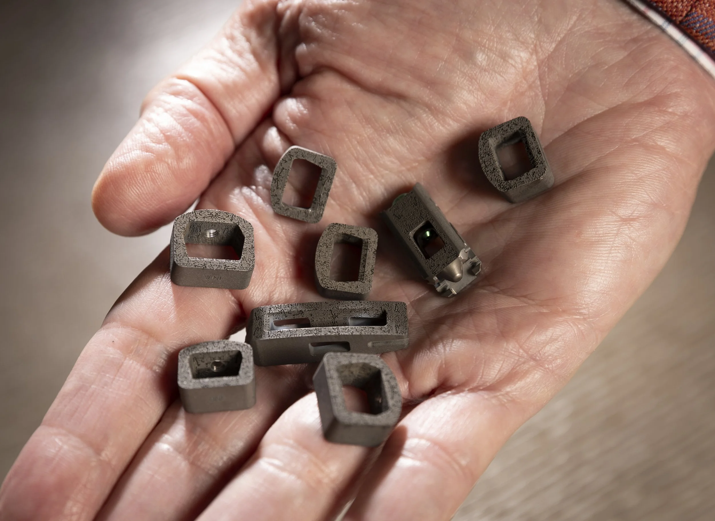 A person's hand holding several small spinal implants with BioBraille nanotechnology with hollow centers, some with internal mechanisms or markings.