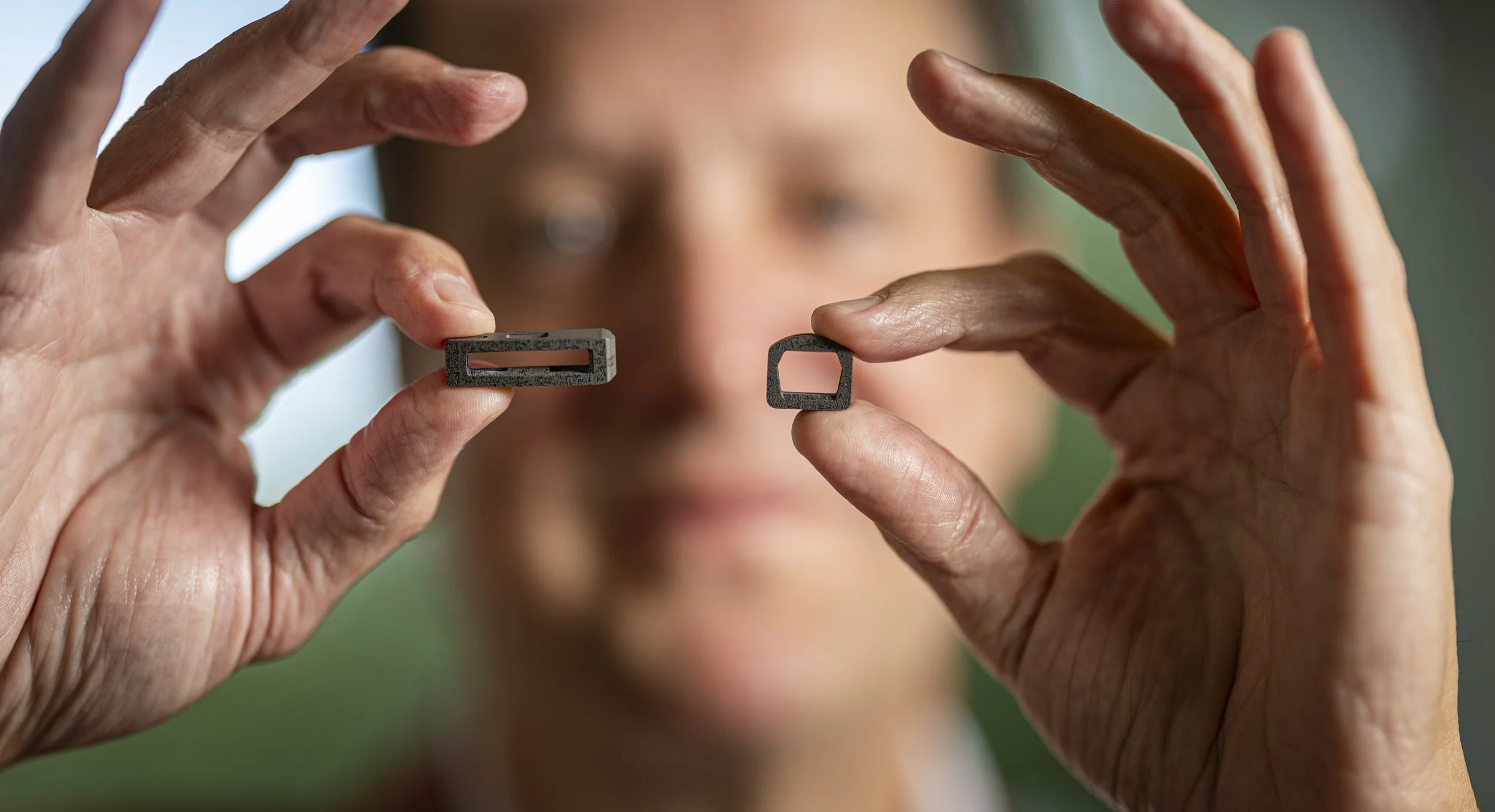 Dr. Robinson holding two small spinal implants with BioBraille nanotechnology, one rectangular with a slot and the other square with open center, close to camera with blurred background.