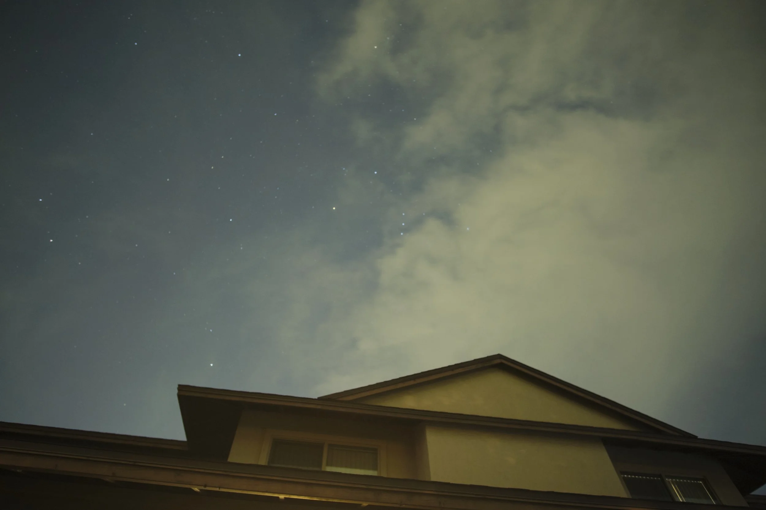 Night sky with stars and clouds above a house roof