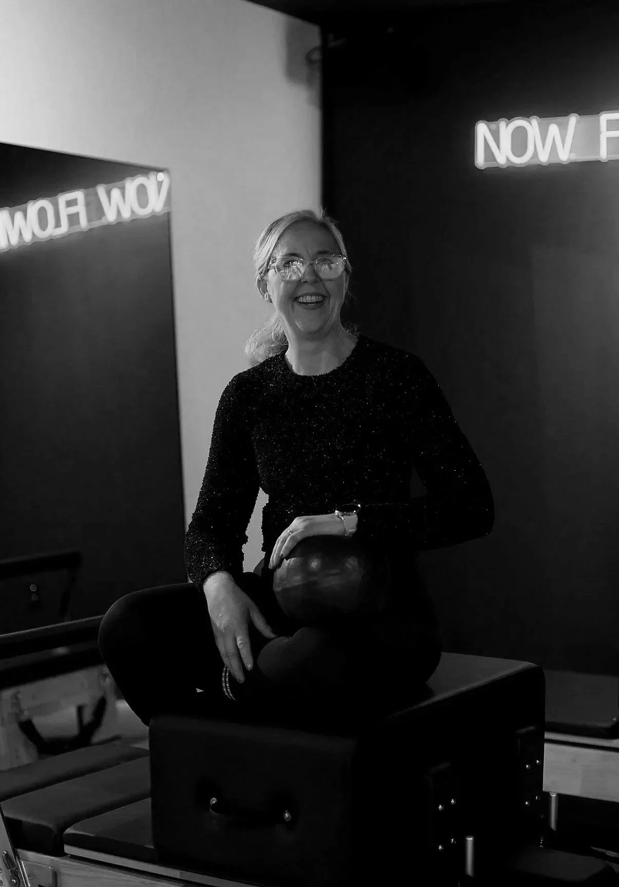 Modern building with wooden and white exterior, large glass window, surrounded by greenery and mountains in the background.