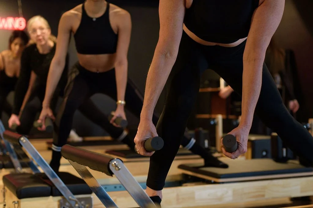 Women participating in a fitness class doing dumbbell exercises on wooden platforms.