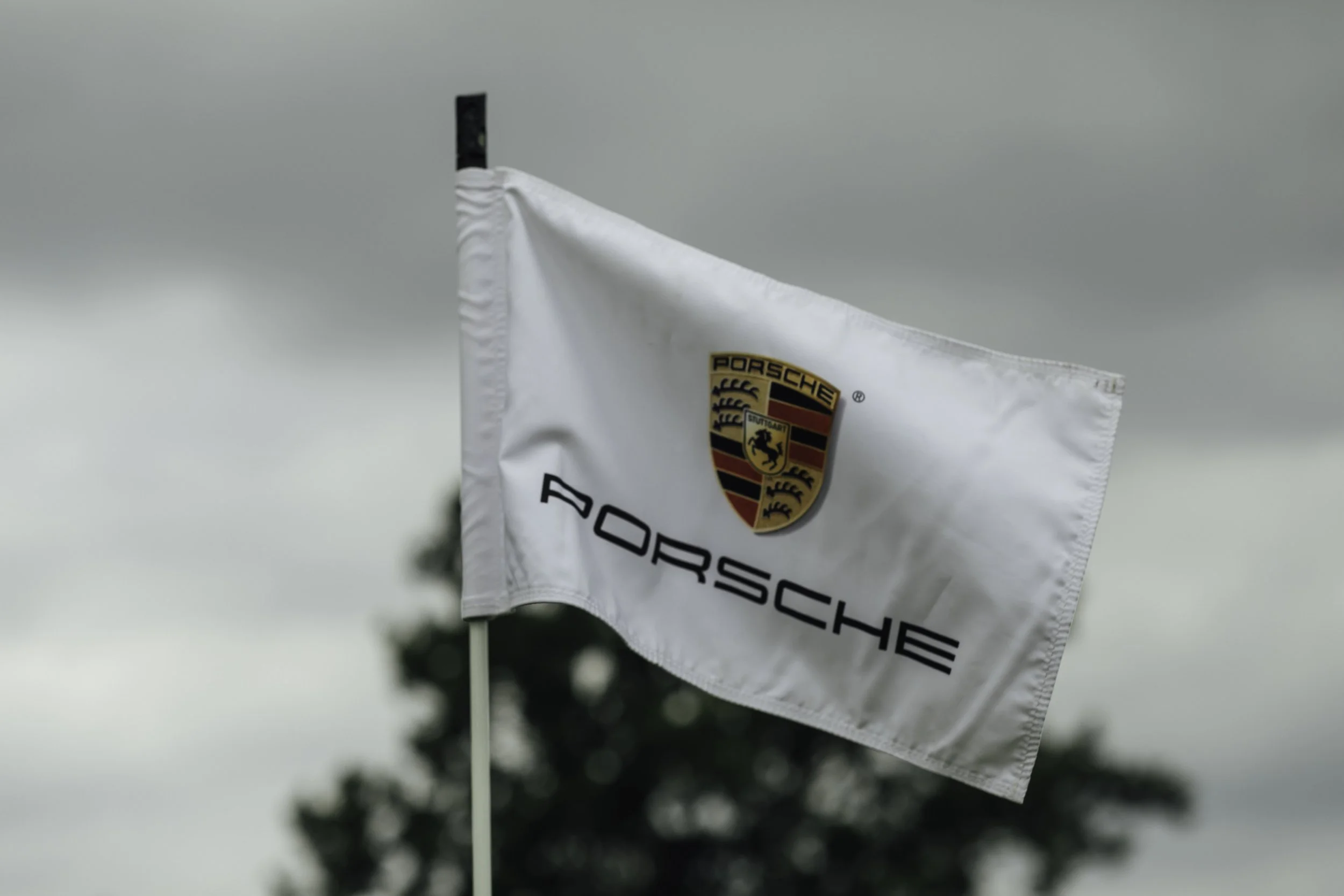 A white flag with the Porsche logo and text, flying outdoors against an overcast sky.
