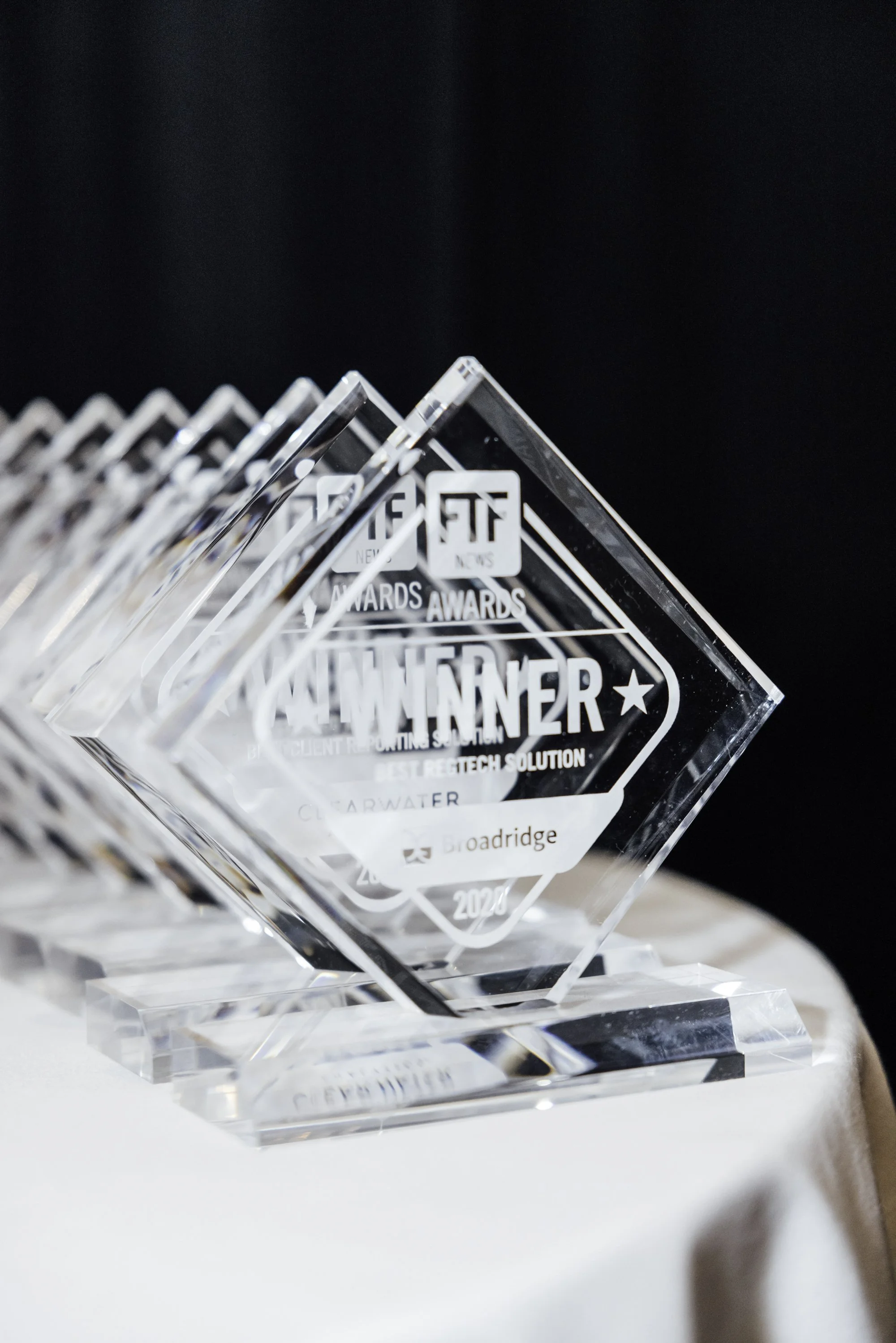A clear glass award with engraved text, displayed on a white surface against a dark background.