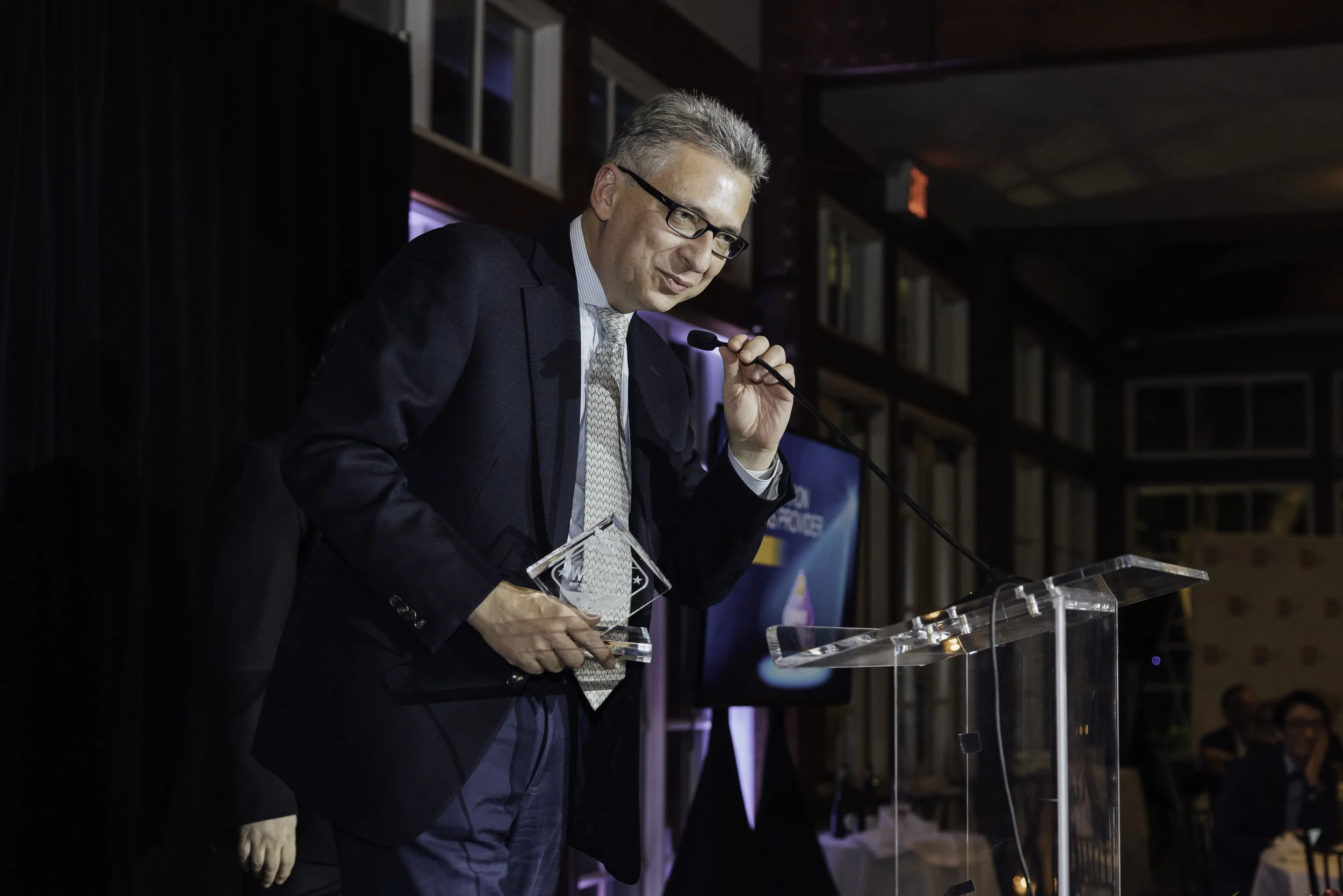 A man in a suit holding a clear award and speaking at a podium during a formal event.