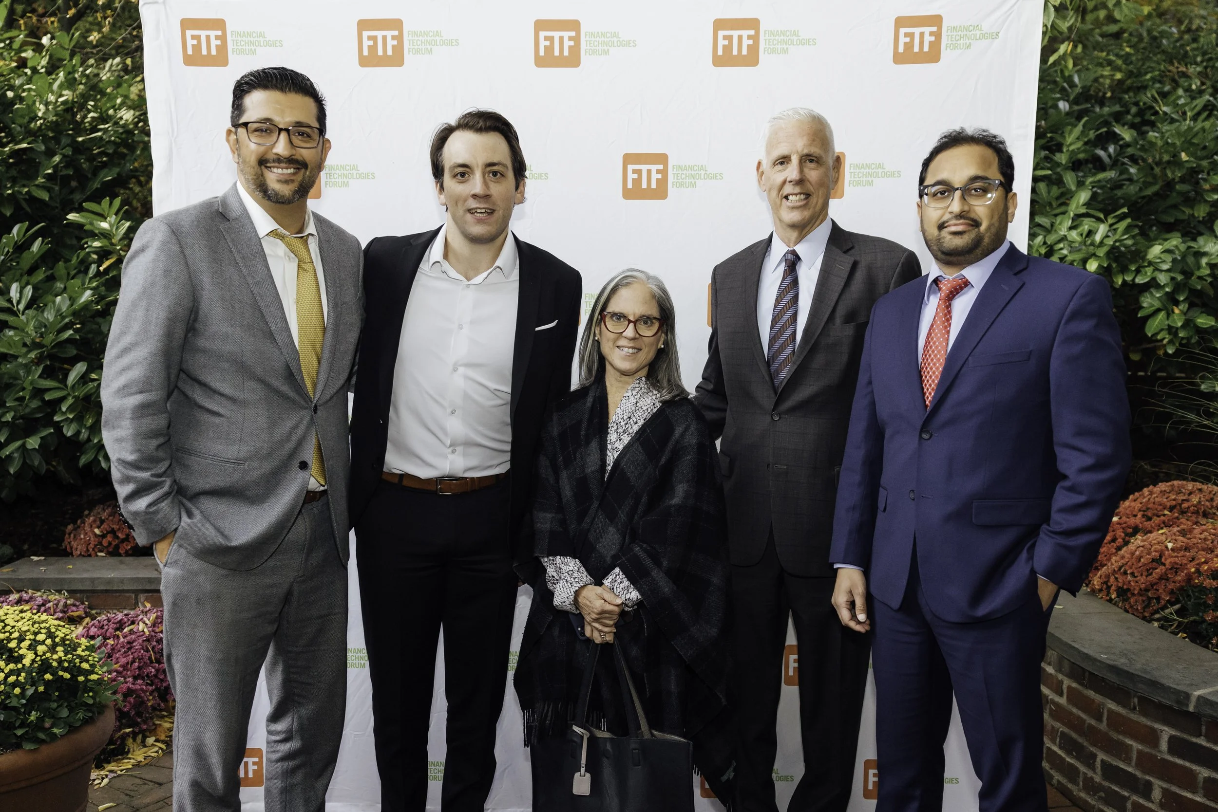 Group of five professionally dressed people standing outdoors in front of a step and repeat banner with the logo for the Financial Technologies Forum (FTF).