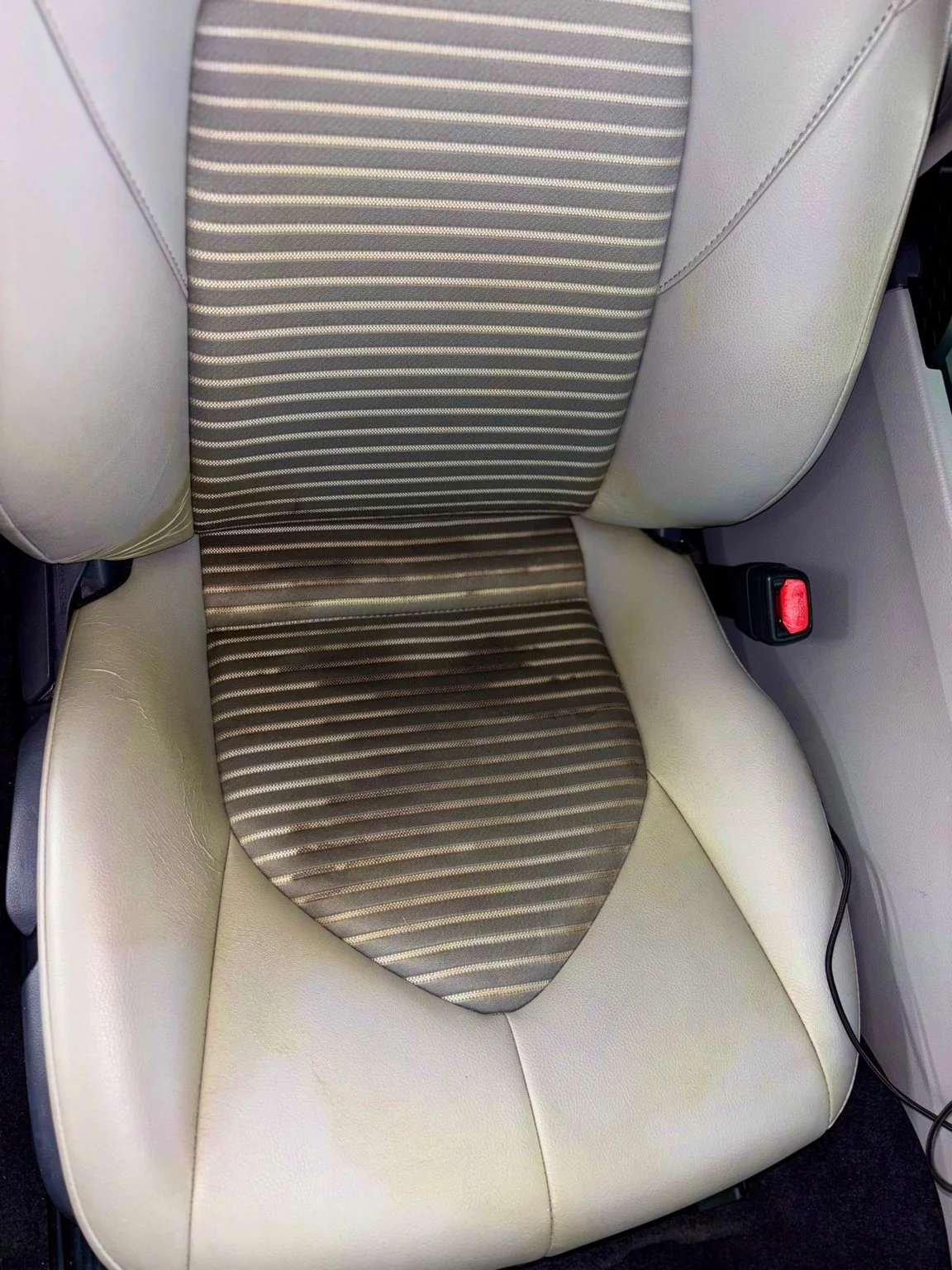 Light leather car seat before interior detailing showing discoloration and surface wear in Naples Florida