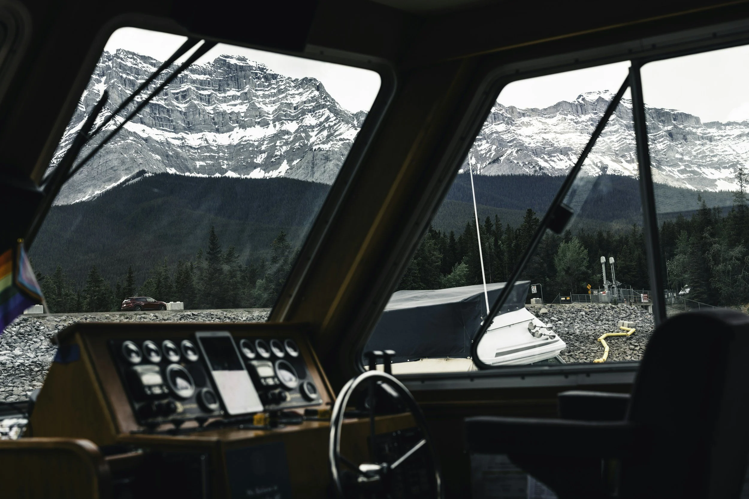 Interior view of a boat with a dashboard, showing mountains, trees, and a boat outside the window.