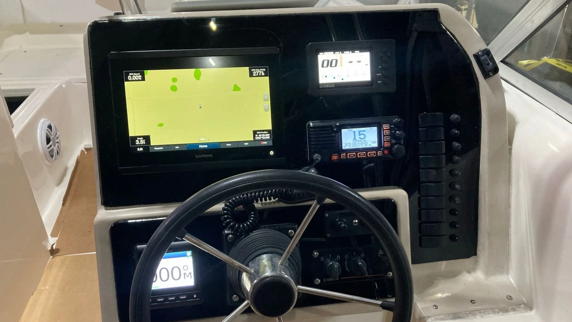The dashboard of a boat with Garmin electronic displays, a Yamaha device, and various controls, with a steering wheel and a marine VHF radio.