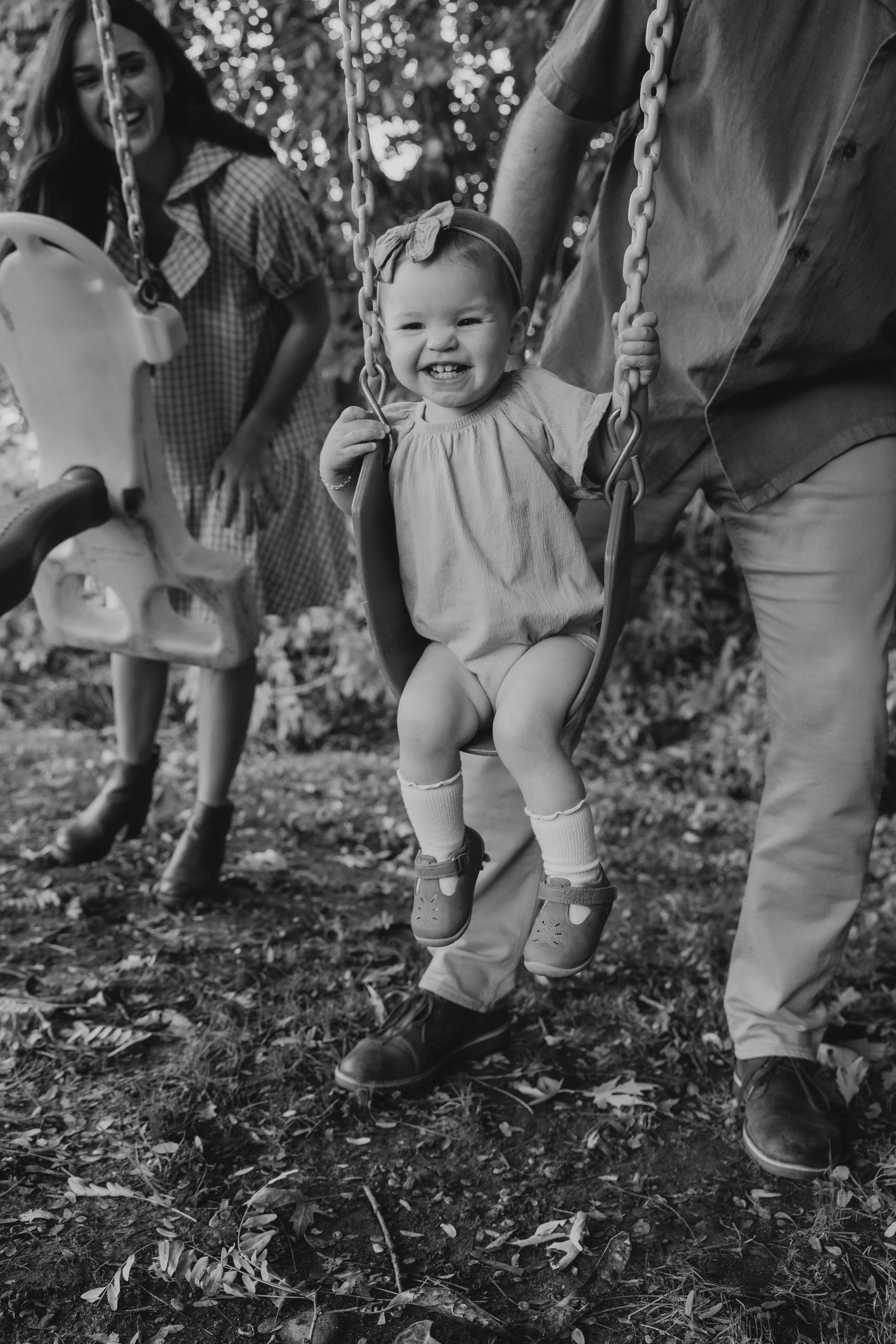 Family playing on a swing set. Young toddler smiling while being pushed by her dad.