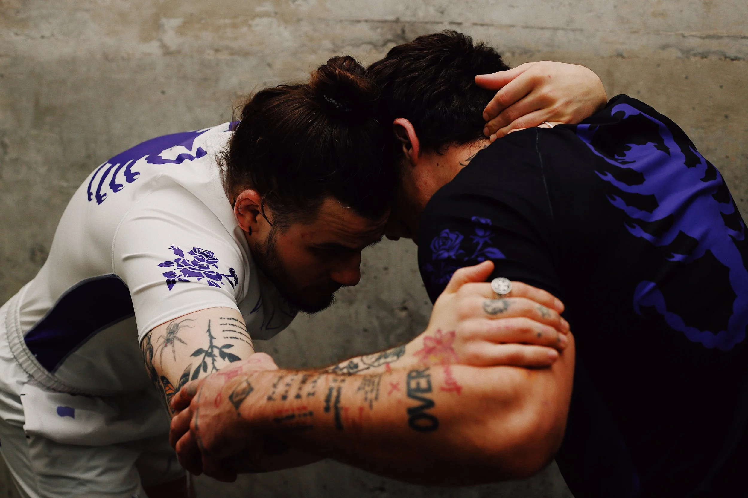 Two men engaging in a traditional arm wrestling match with their foreheads touching, showing intense effort and concentration.