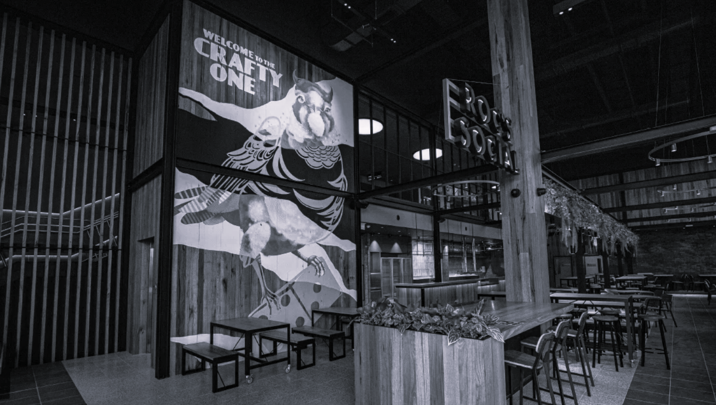 Interior of a modern bar or restaurant with wooden decor, a large mural of a bird with the text  and a seating area with high chairs and tables.