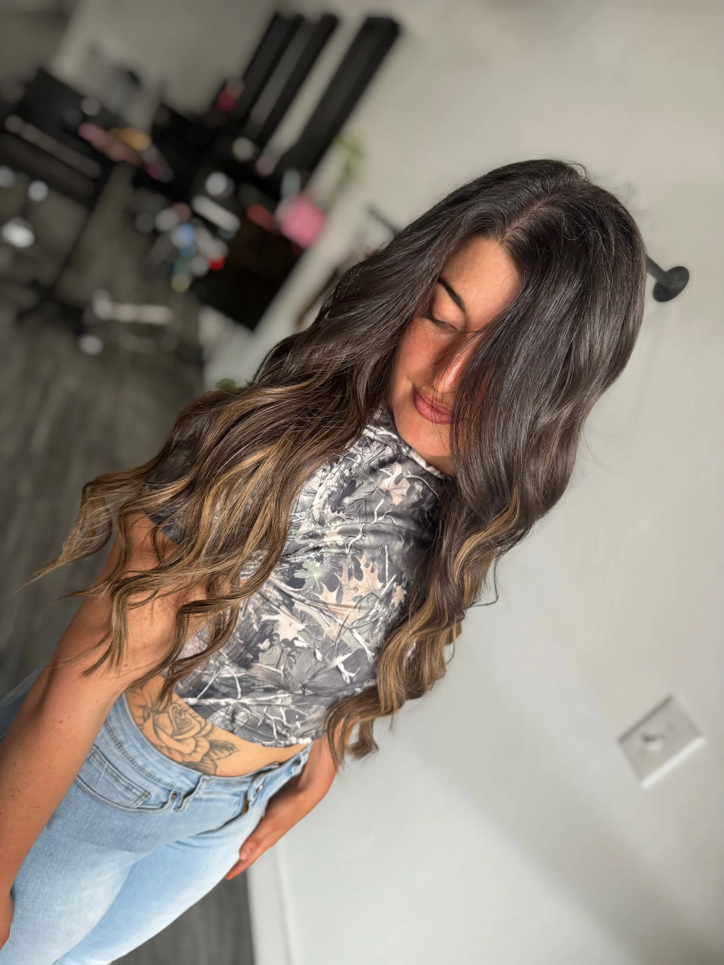 Woman with long wavy hair and a floral crop top standing indoors.