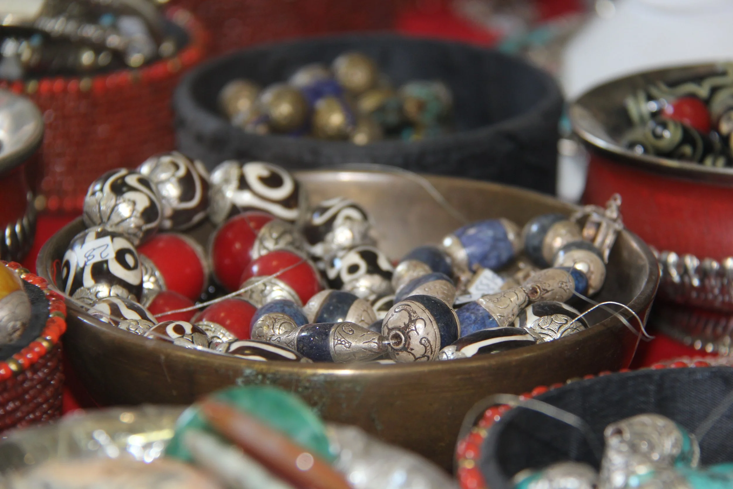 Close-up of various jewelry pieces including beads, rings, and pendants displayed in bowls at a market or jewelry stall.