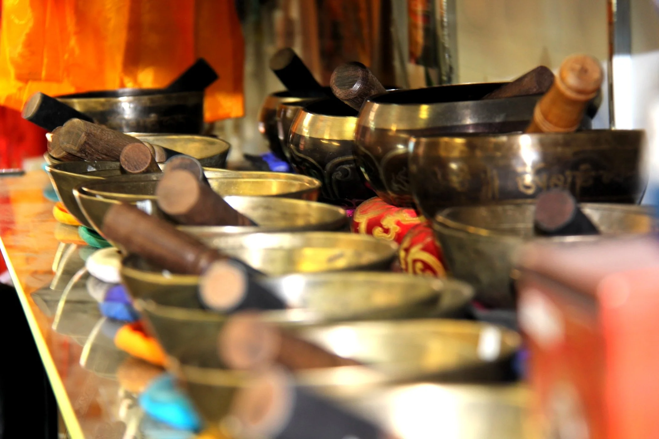 Multiple singing bowls with mallets on a shelf in a shop or marketplace.