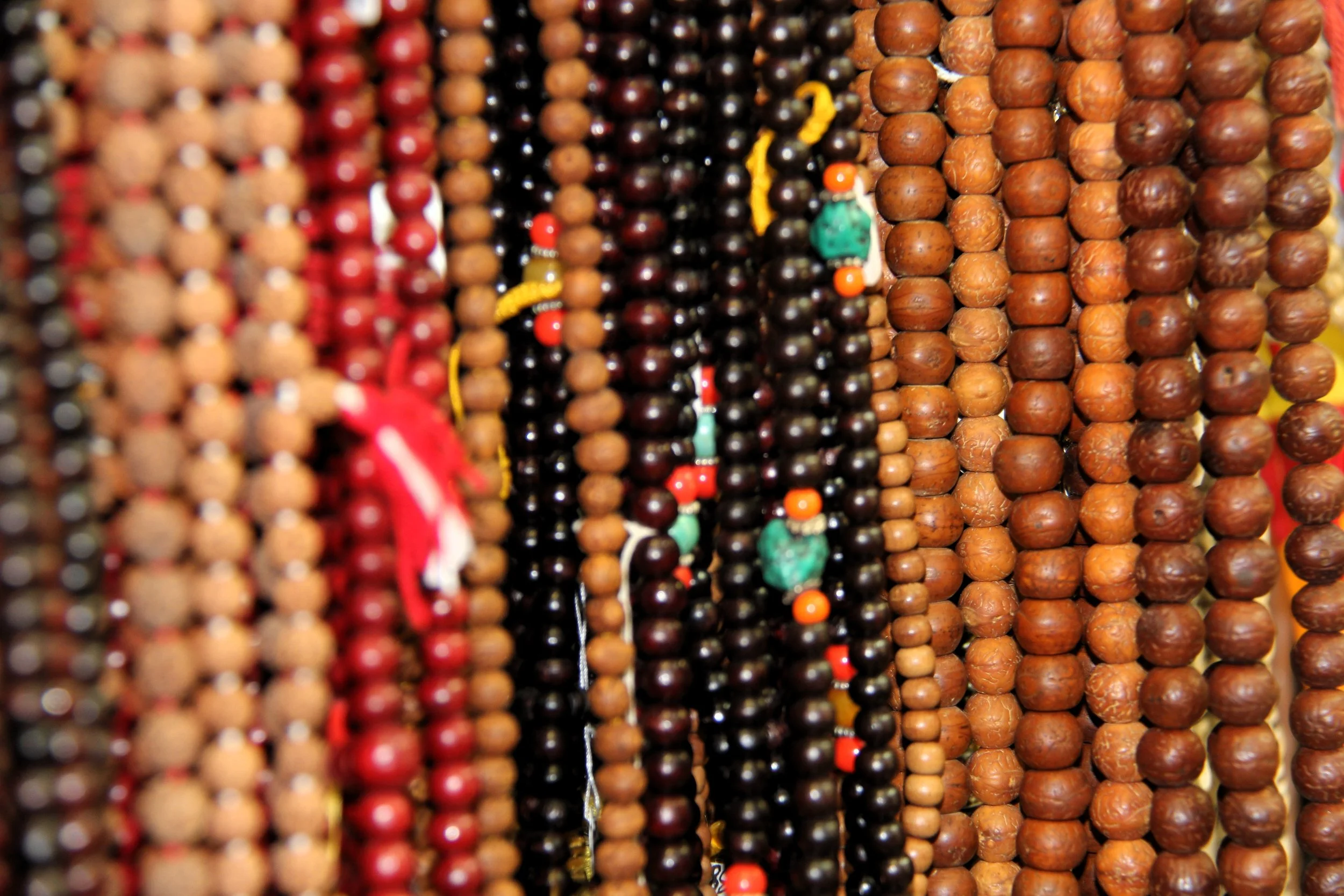 Close-up of multiple strands of beads in various colors and sizes, hanging together.