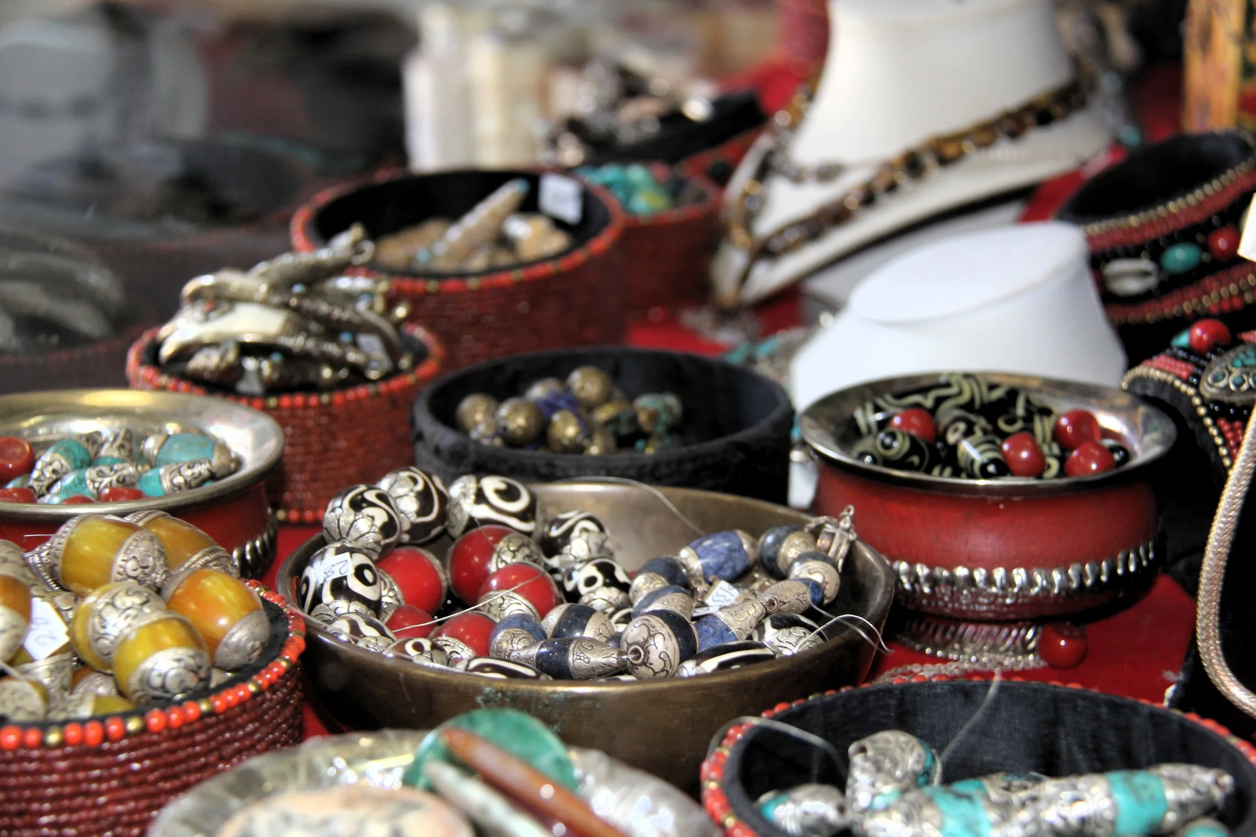 Display of various jewelry items including beaded bracelets, necklaces, and earrings in colorful bowls and containers.