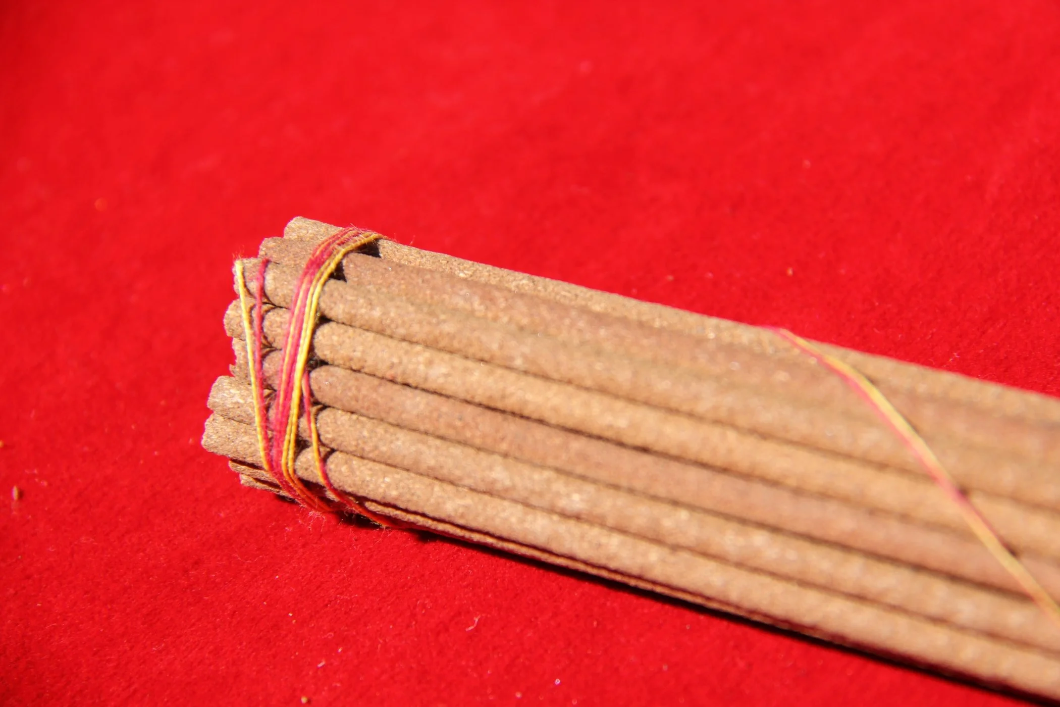 Bundle of cinnamon sticks tied together with a rubber band on a red surface.