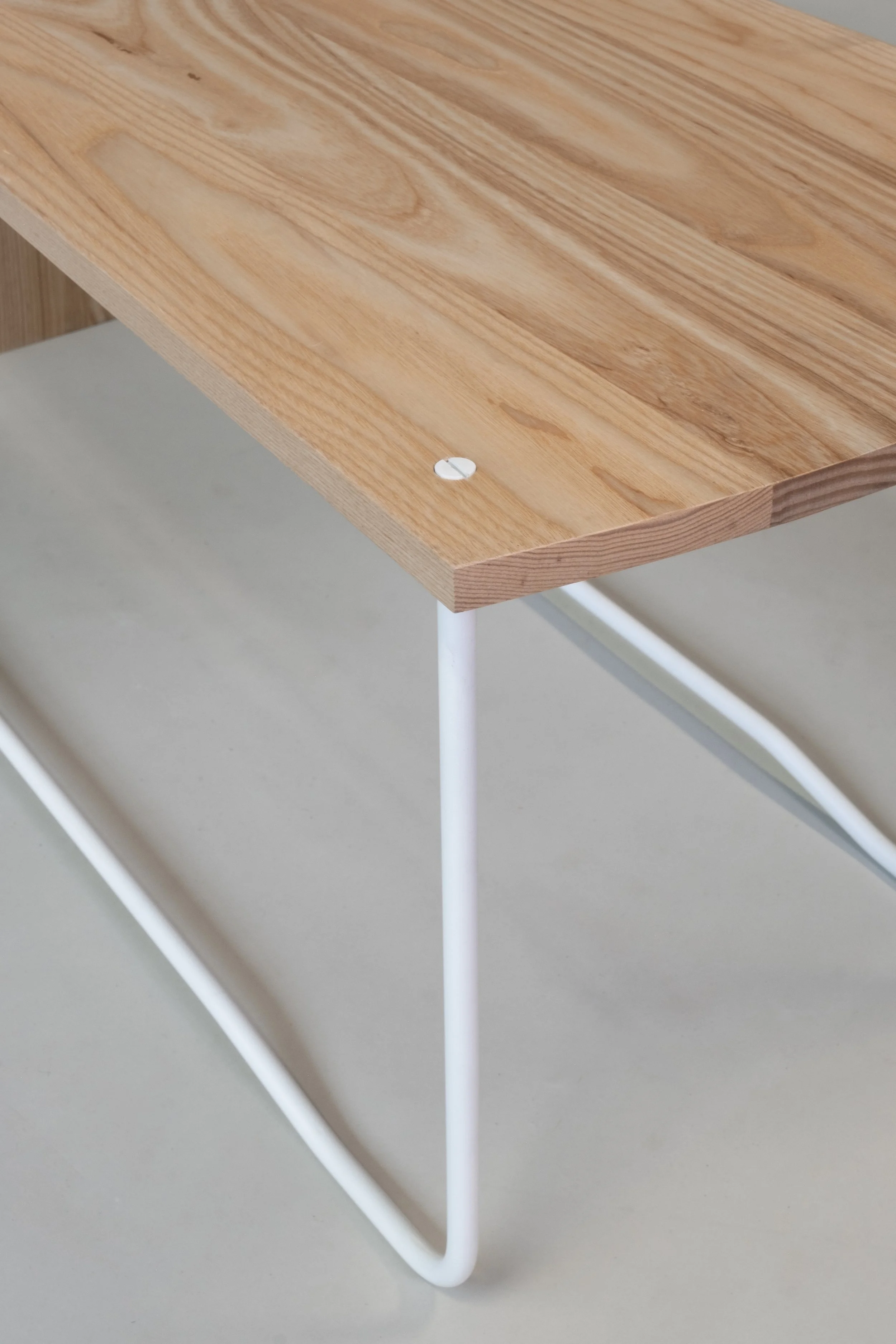 Close-up of a wooden table edge with a screw, supported by white metal legs on a gray floor.