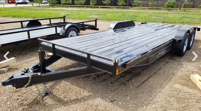 Black flatbed trailer with dual axles parked on gravel, with a hitch and safety chains at the front.