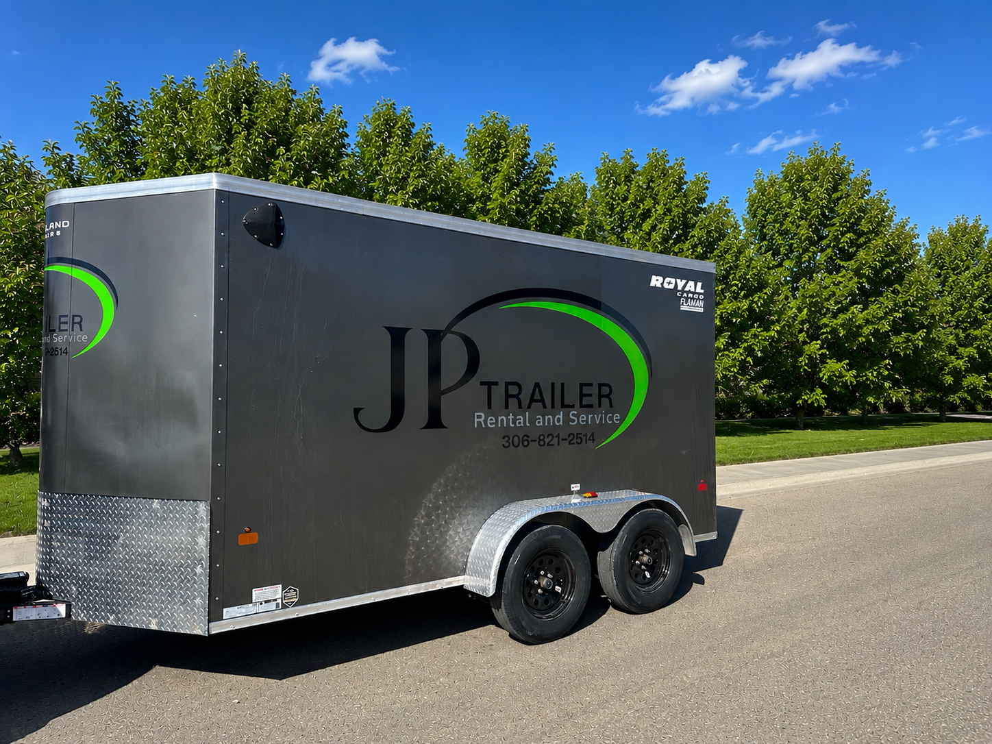A black trailer with the branding 'JP Trailer Rental and Service' parked on a street with green trees and a blue sky in the background.