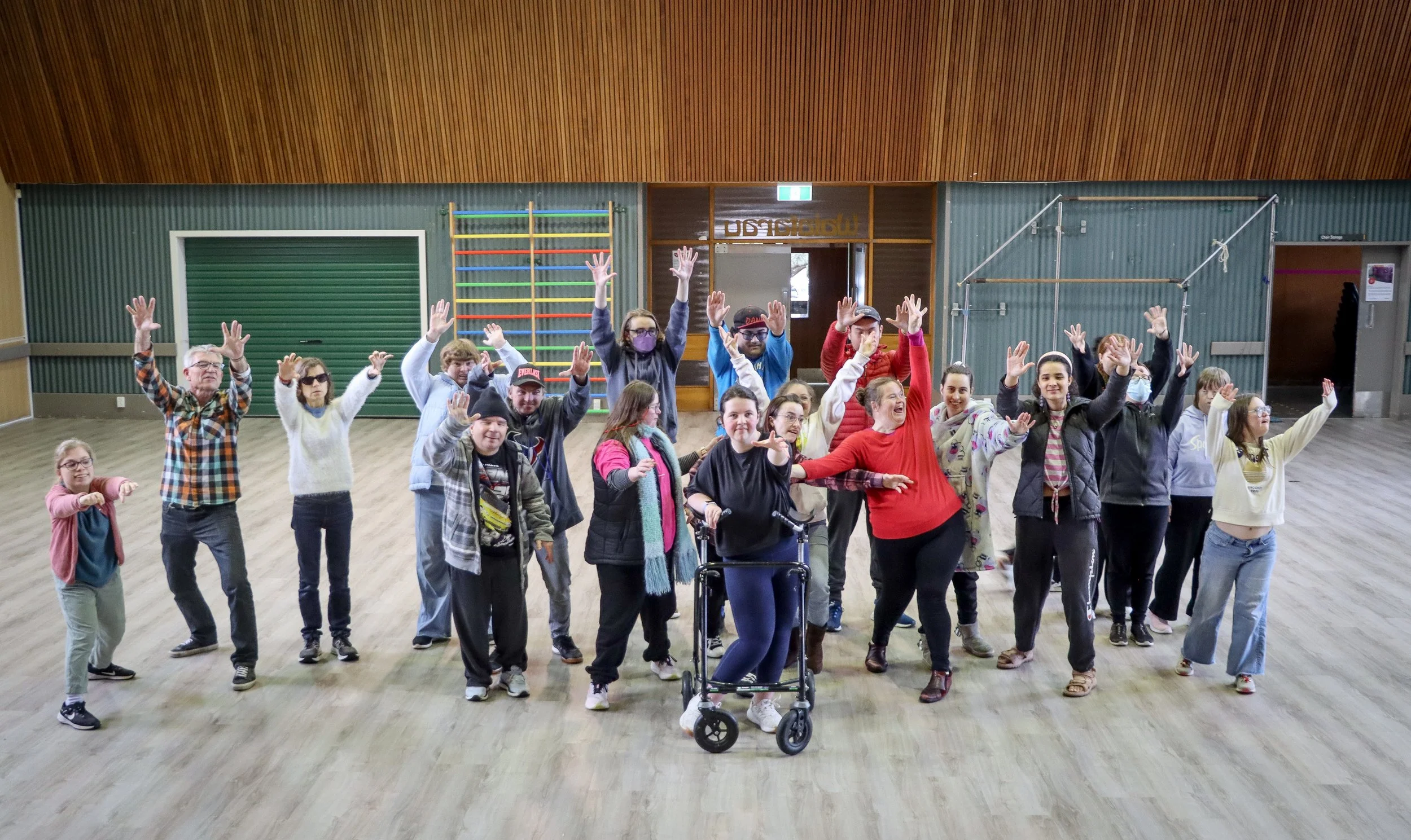 Group of people of various ages raising their arms inside a large multi-purpose room.