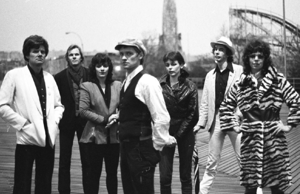 A black-and-white photo of seven people standing outdoors with a bridge visible in the background.