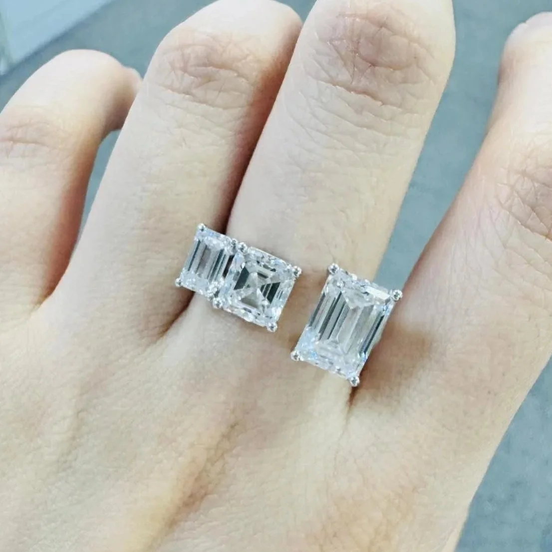 A hand wearing a Toi et Moi ring with two large square-shaped diamond rings on the ring.