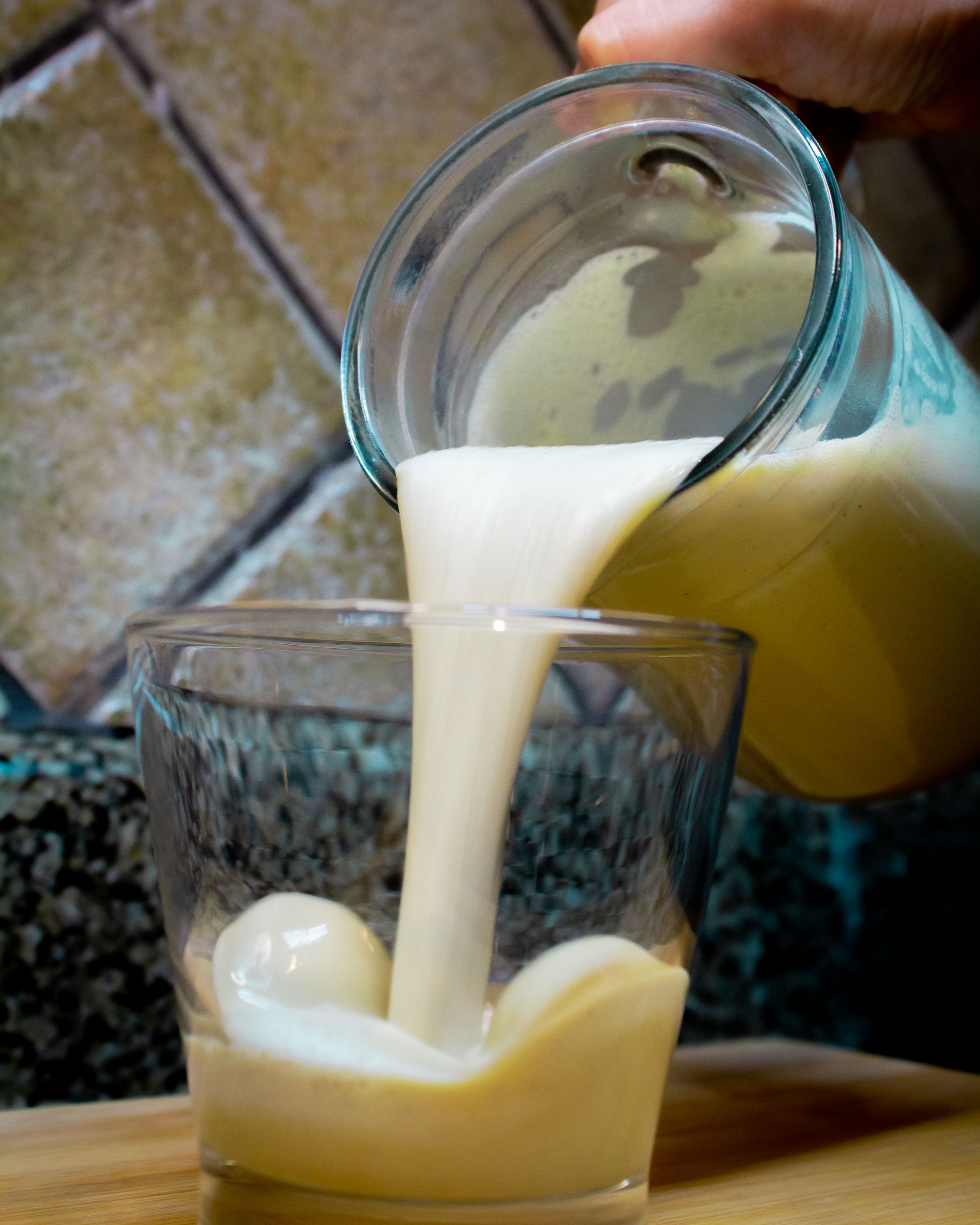Vaso siendo lleno con rompope plant-based. Fondo con azulejos de cerámica.