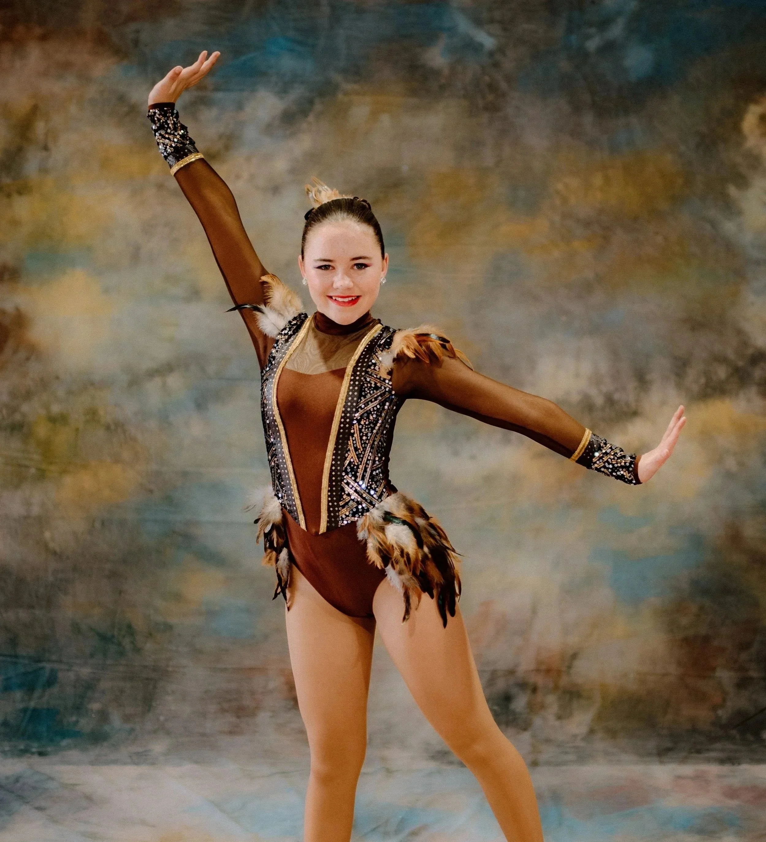 Young woman in athletic attire performing a breakdancing move on a studio floor, with one hand on the ground and her other arm raised.