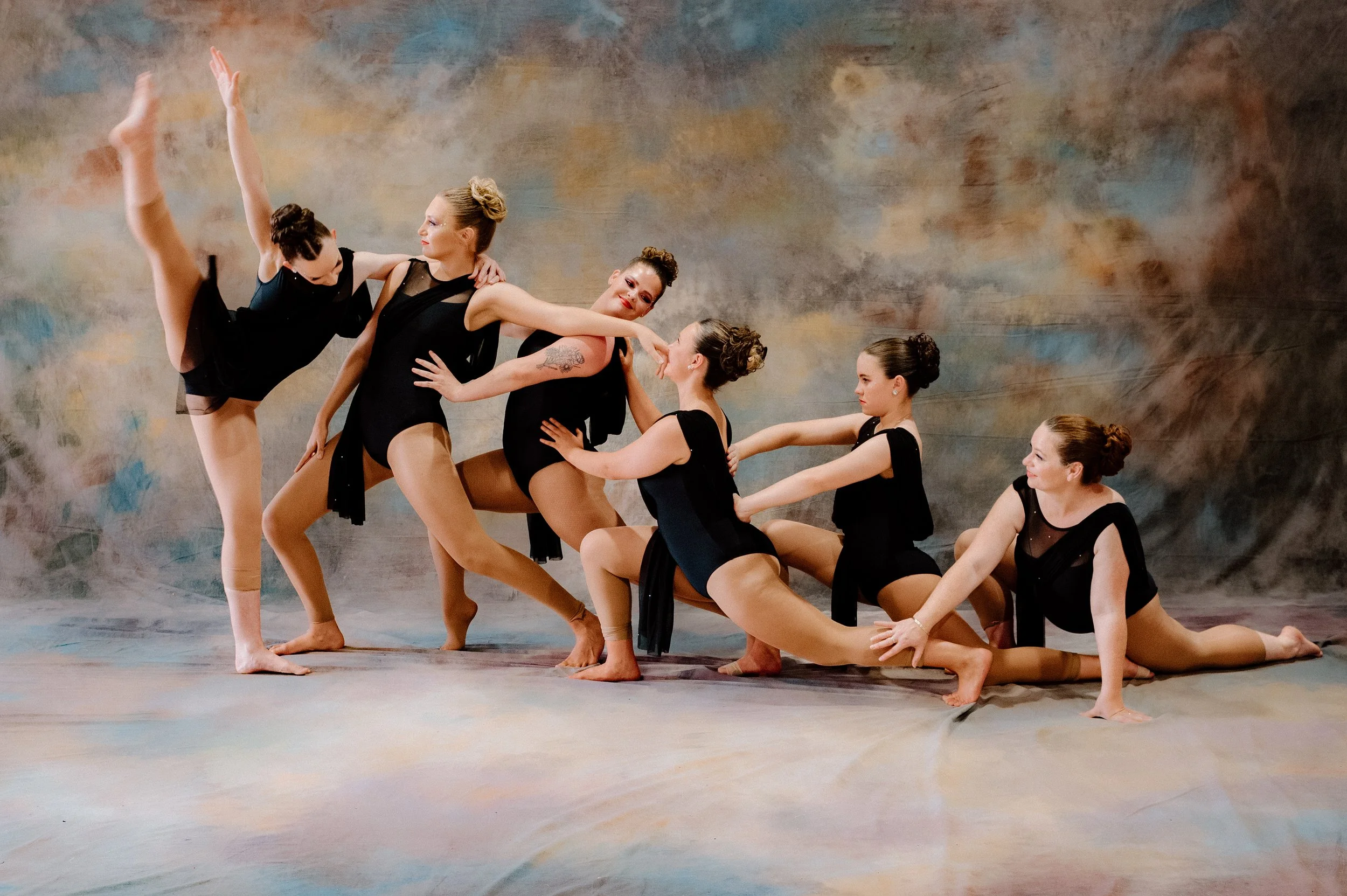 A group of young female dancers in bright orange costumes posing together in a studio.
