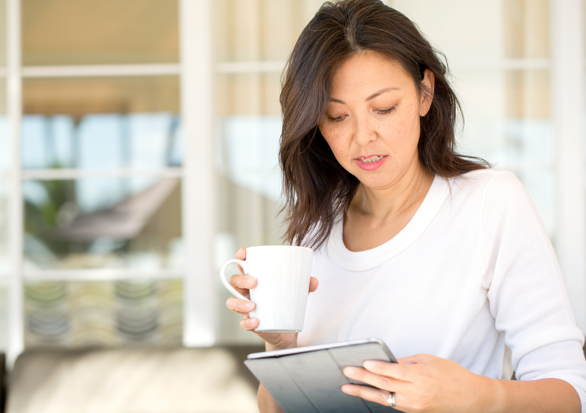 Woman reading journal on ipad with cup of tea