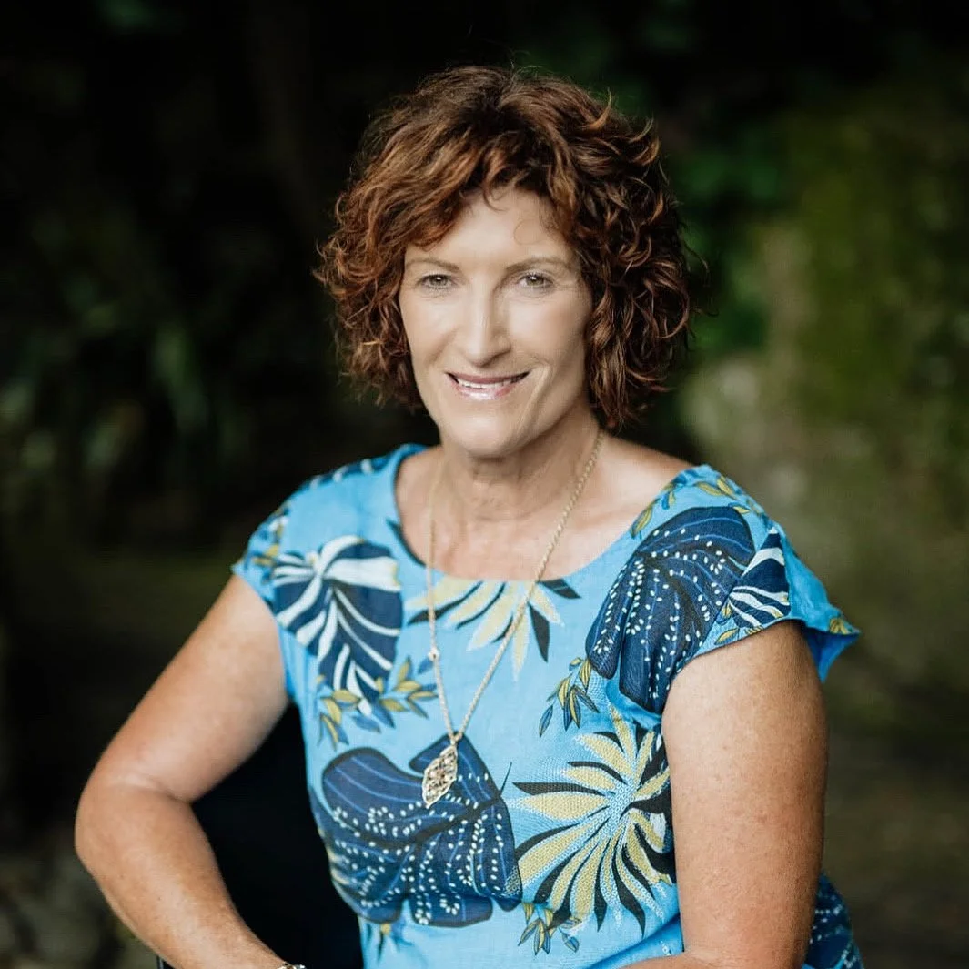 Maria Balan smiling outdoors, wearing a blue floral dress and a gold necklace.