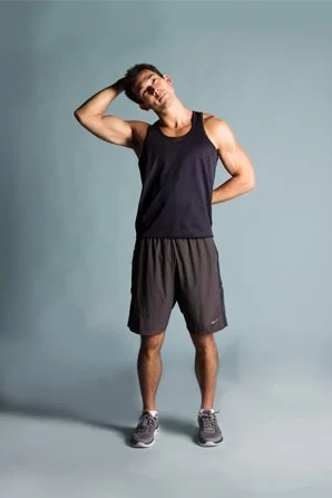 Young man in athletic clothing stretching or adjusting his hair against a gray background.