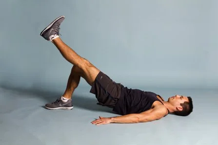 Man performing leg lifts lying on the floor in a fitness studio