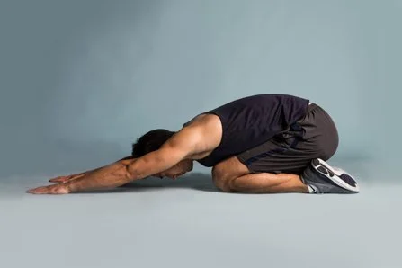 Man in a yoga pose kneeling with arms extended forward on the ground