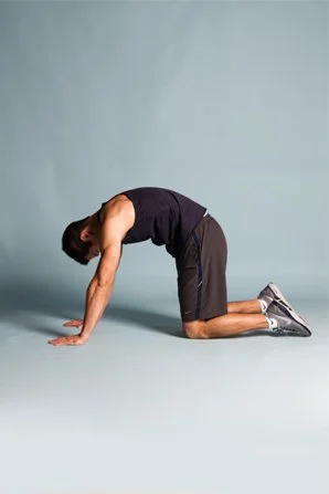 Man in black sleeveless shirt and shorts performing a yoga pose on the floor.