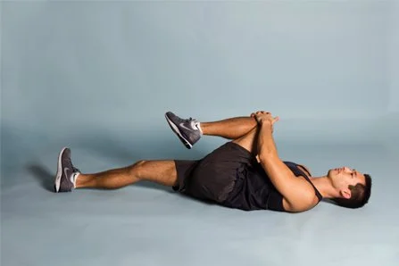 Woman lying on her back stretching her legs and arms in a fitness studio with a plain blue background.