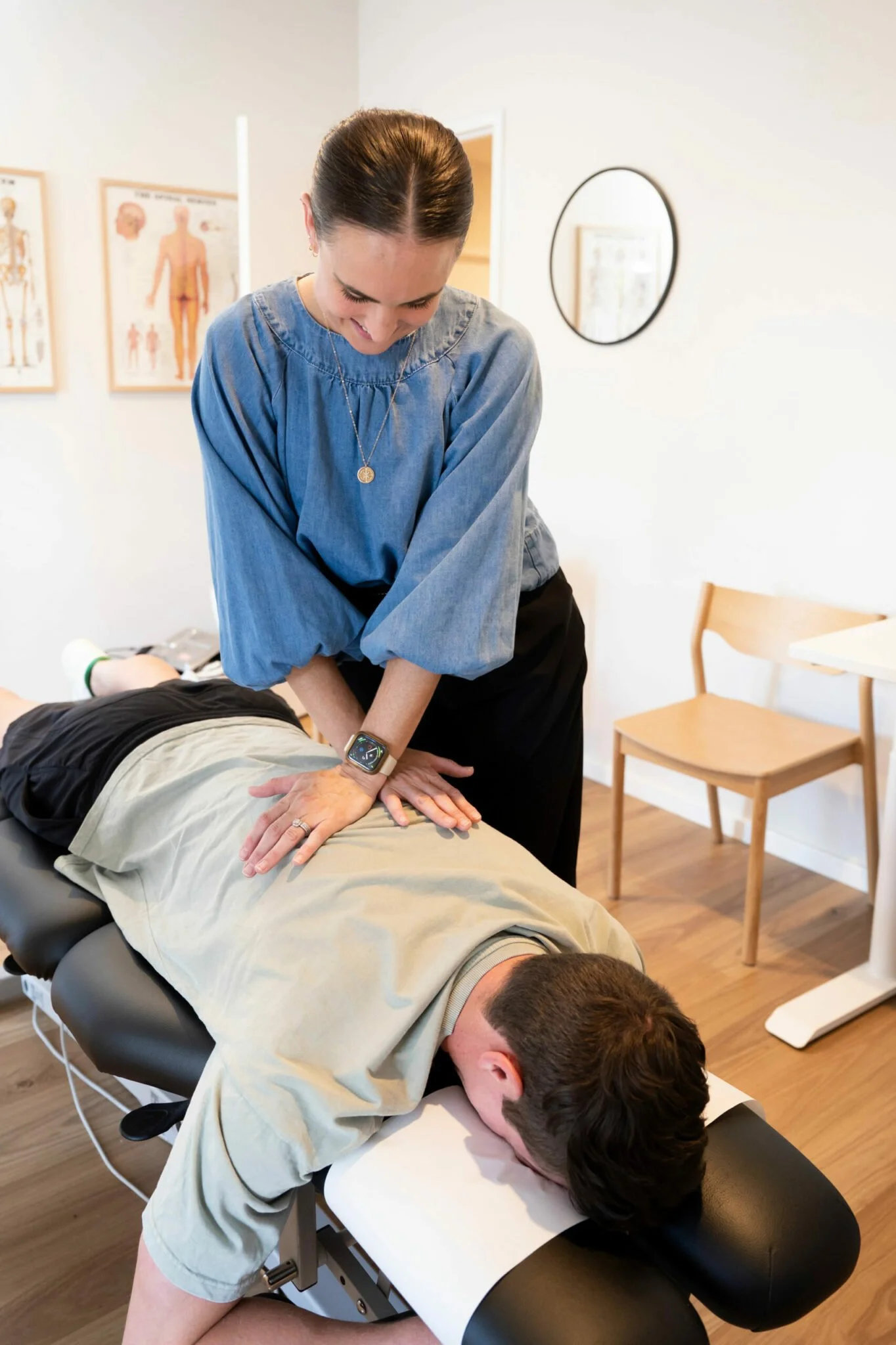 A woman performing chiropractic adjustment on a man lying face down on a chiropractic table in a medical office.