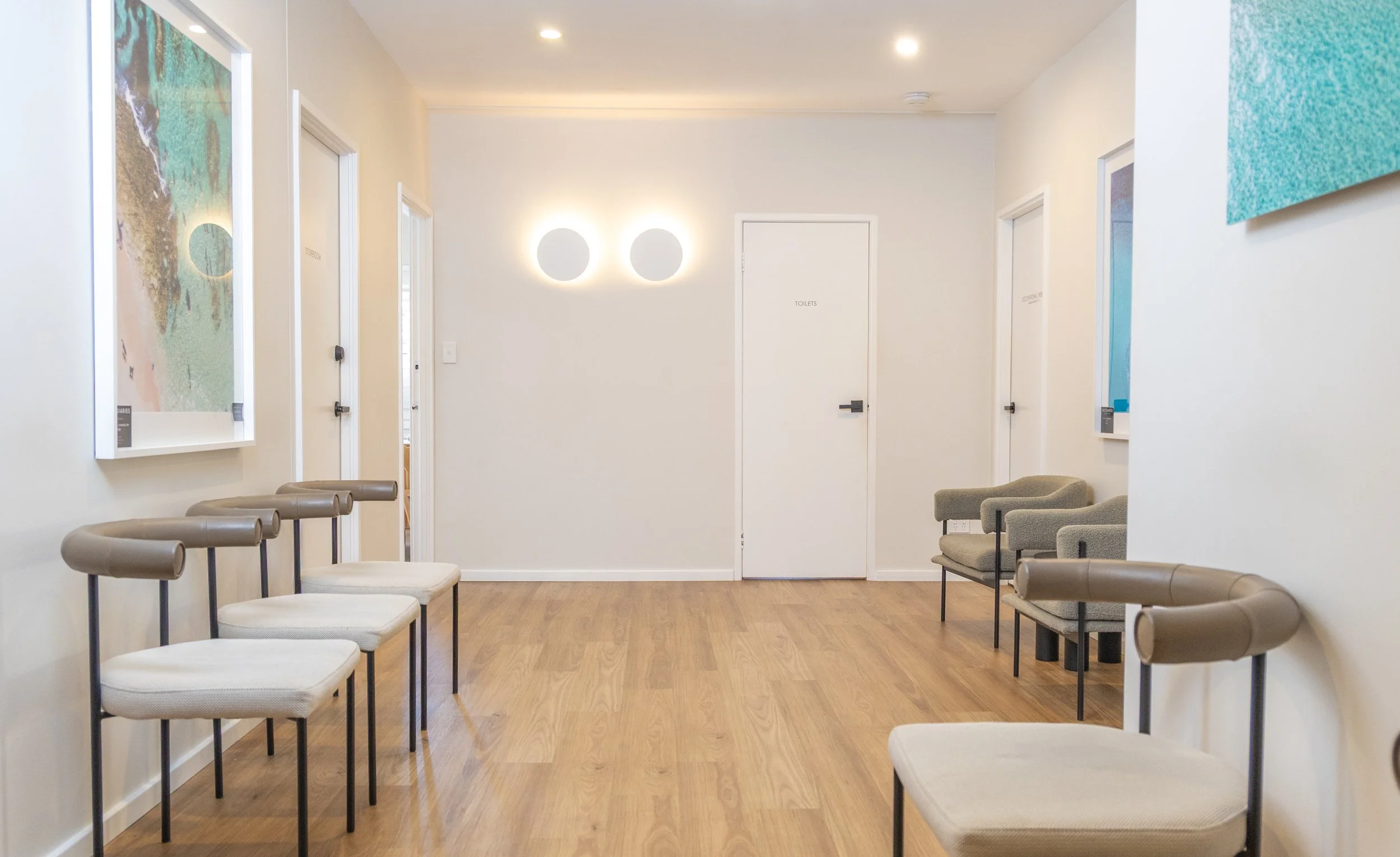 Waiting area with chairs along the walls, artwork on the walls, and a door labeled 'TOILETS' in the background.