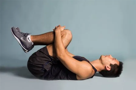 A man lying on his back holding his knees to his chest in a stretching exercise.