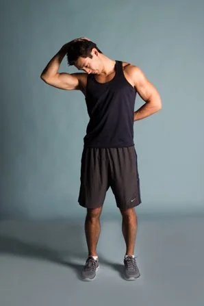 Young man in athletic wear scratching his head and looking down against a plain background.