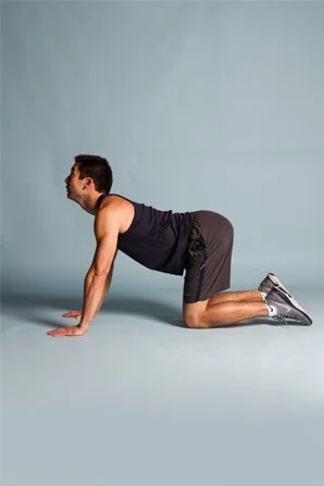 Man in athletic clothing on hands and knees, stretching or exercising against a light blue background.