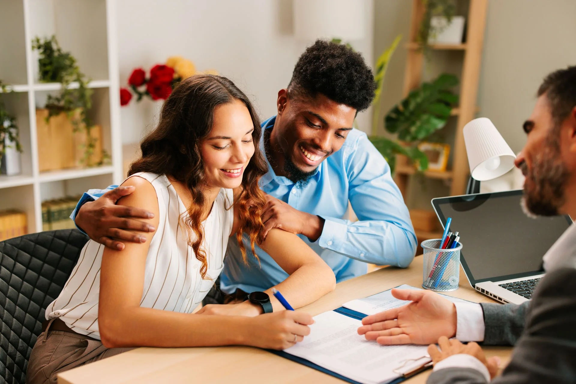 A happy couple signing home loan documents with a man in a business suit notarizing.