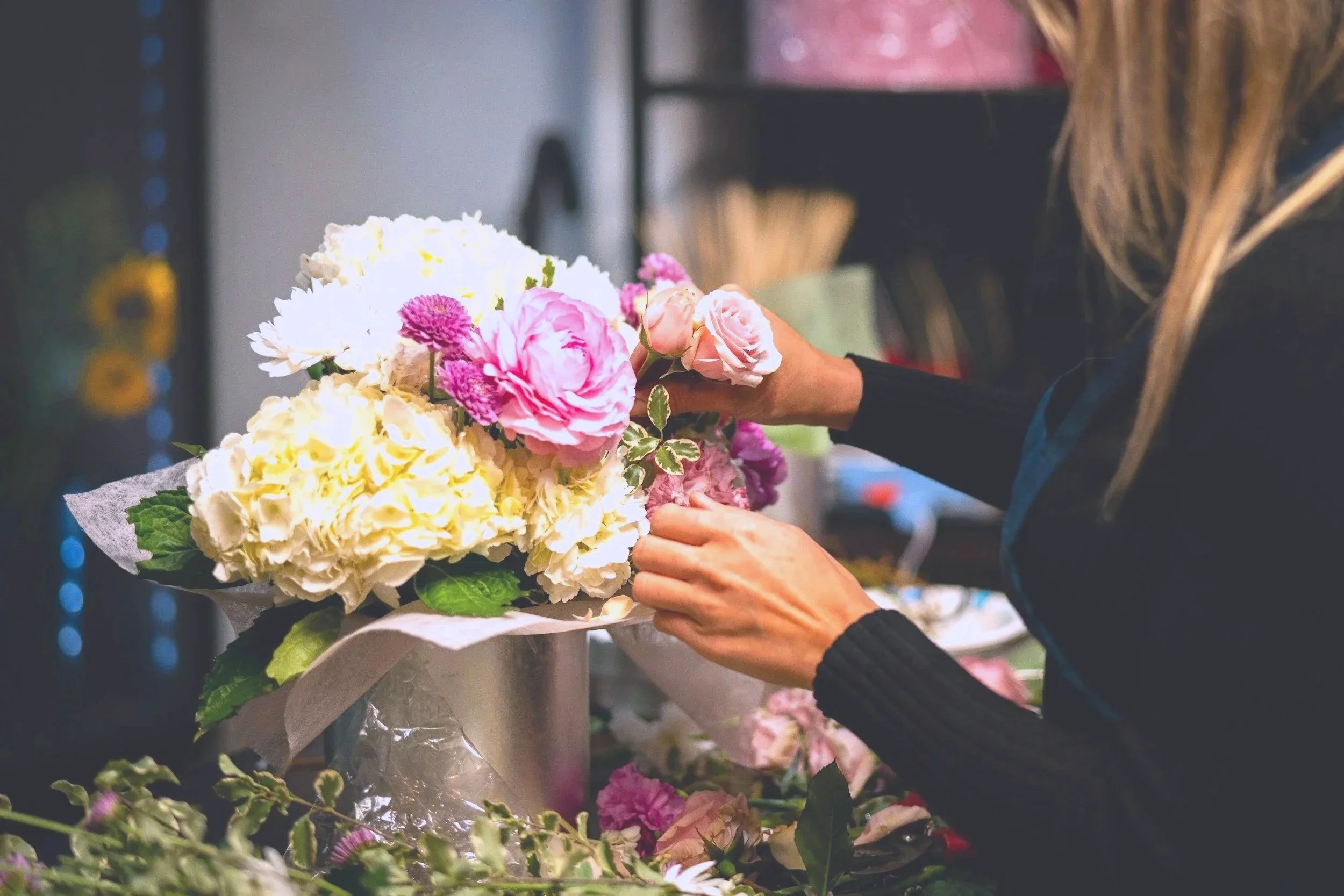 A florist arranging a bouquet of pink, white, and purple flowers in a Floral Studio.