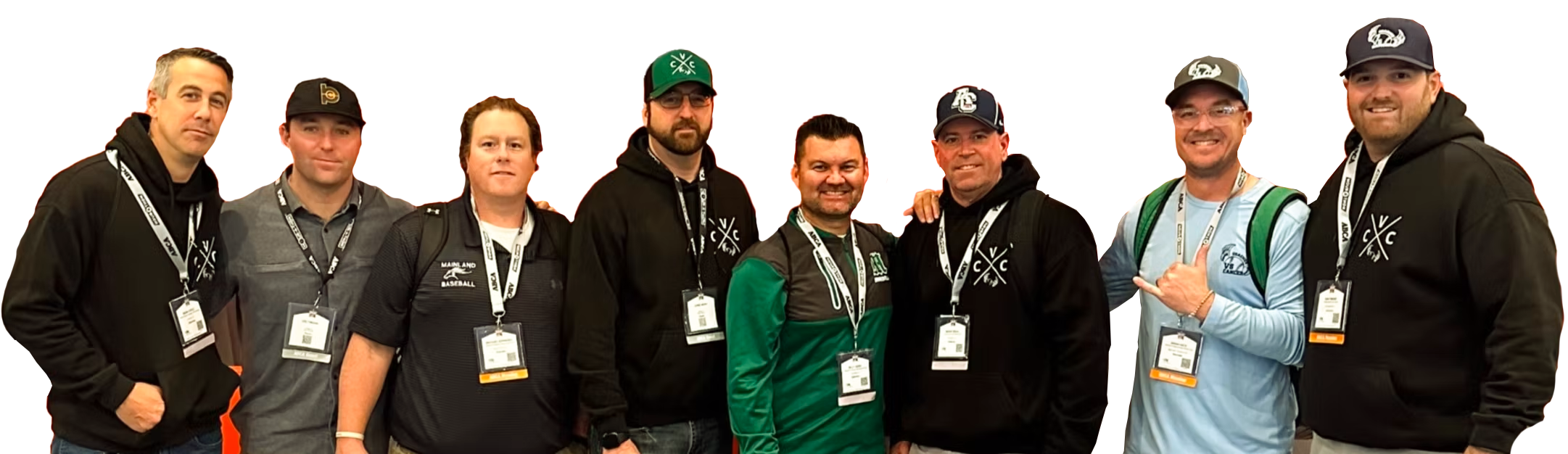 Group of eight men standing together at an event, wearing casual and team apparel with event badges around their necks.